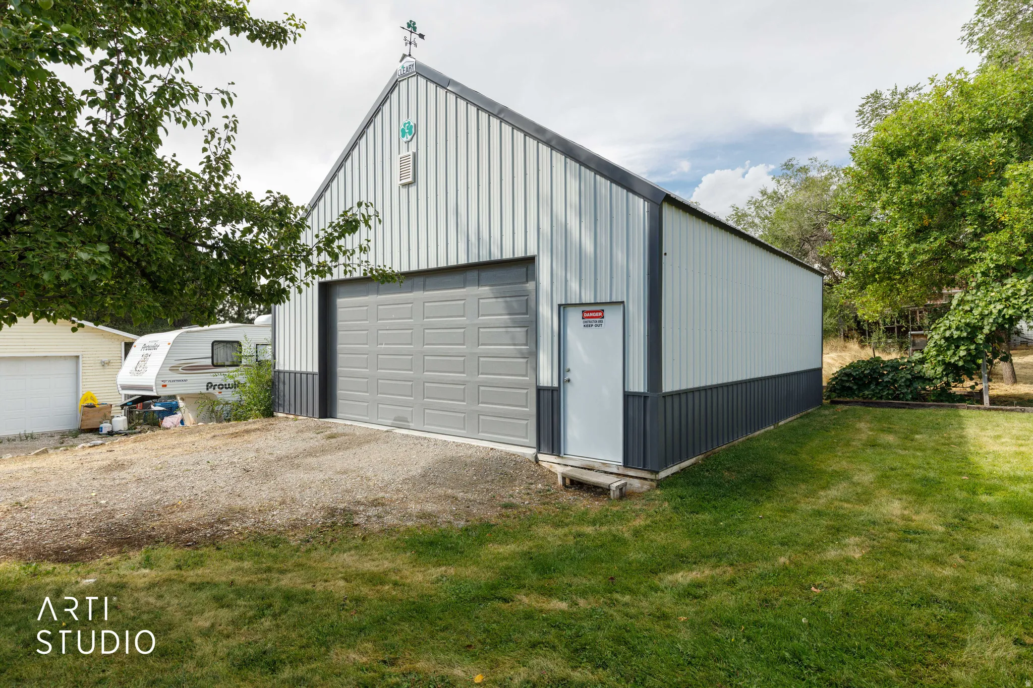Metal sided shop featuring a gray overhead door, white side entry door, and a weather vane accent