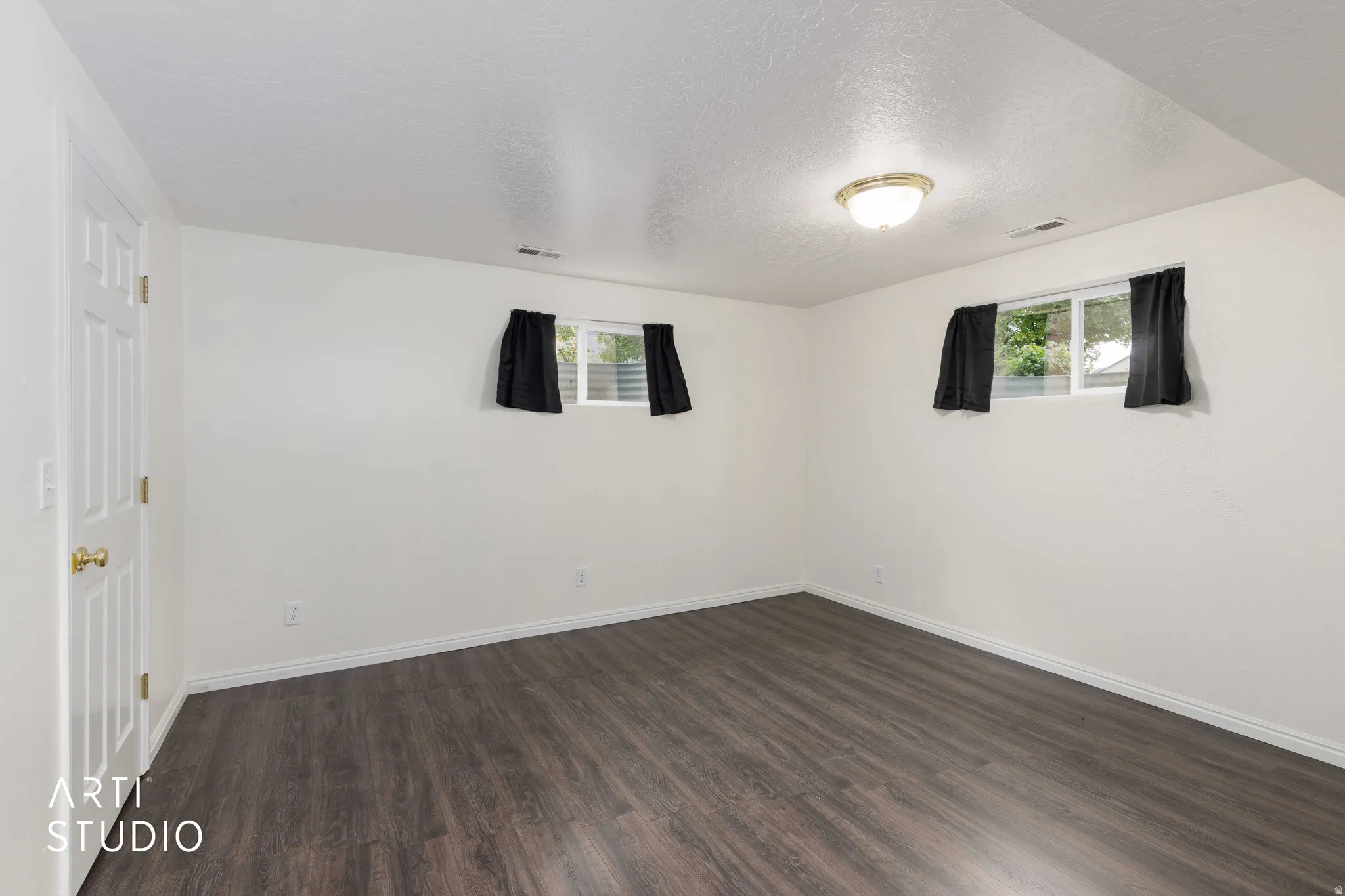White interior walls, wood-finish flooring, two windows, and a flush-mount ceiling light fixture