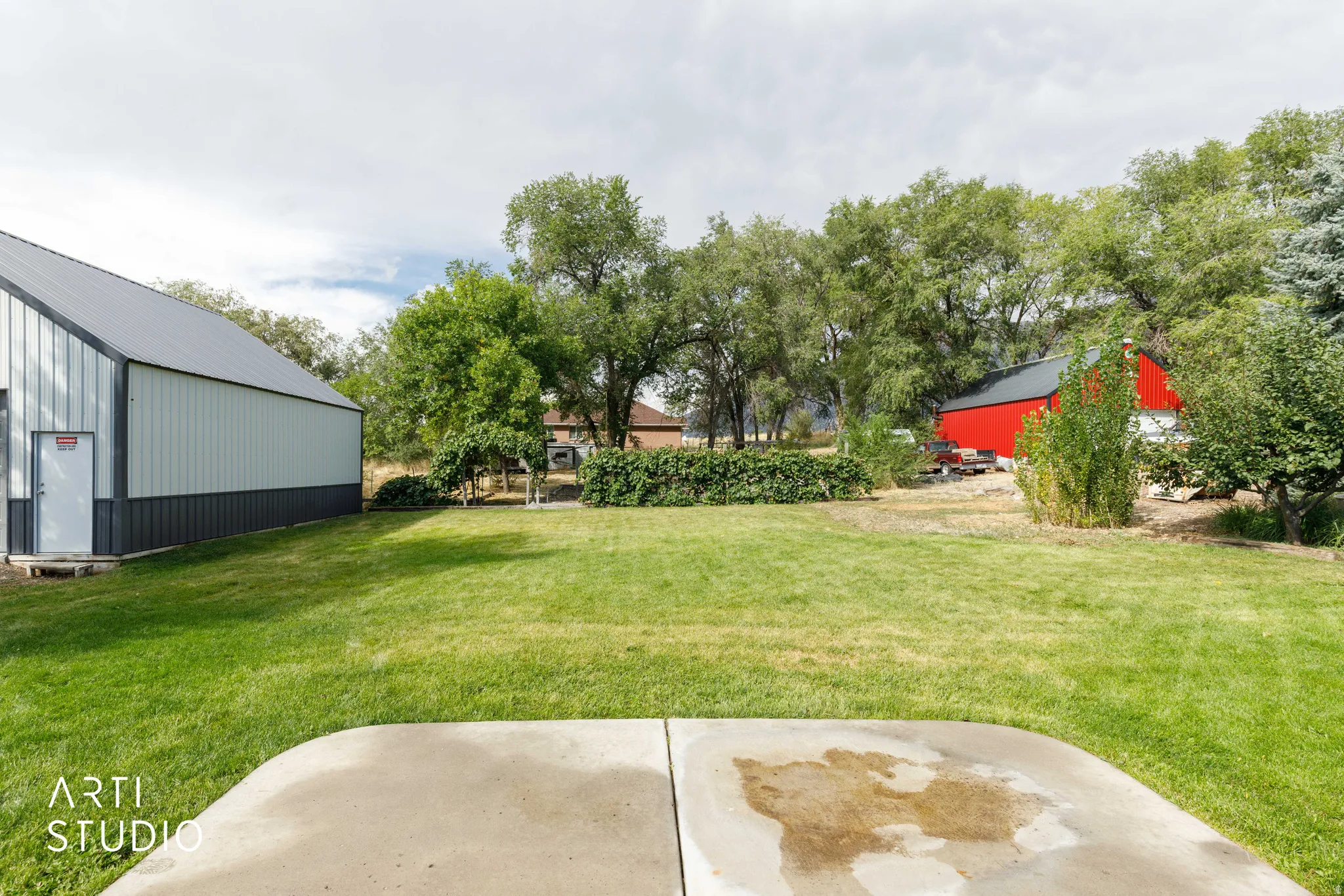 Expansive grassy area with mature trees and a concrete patio