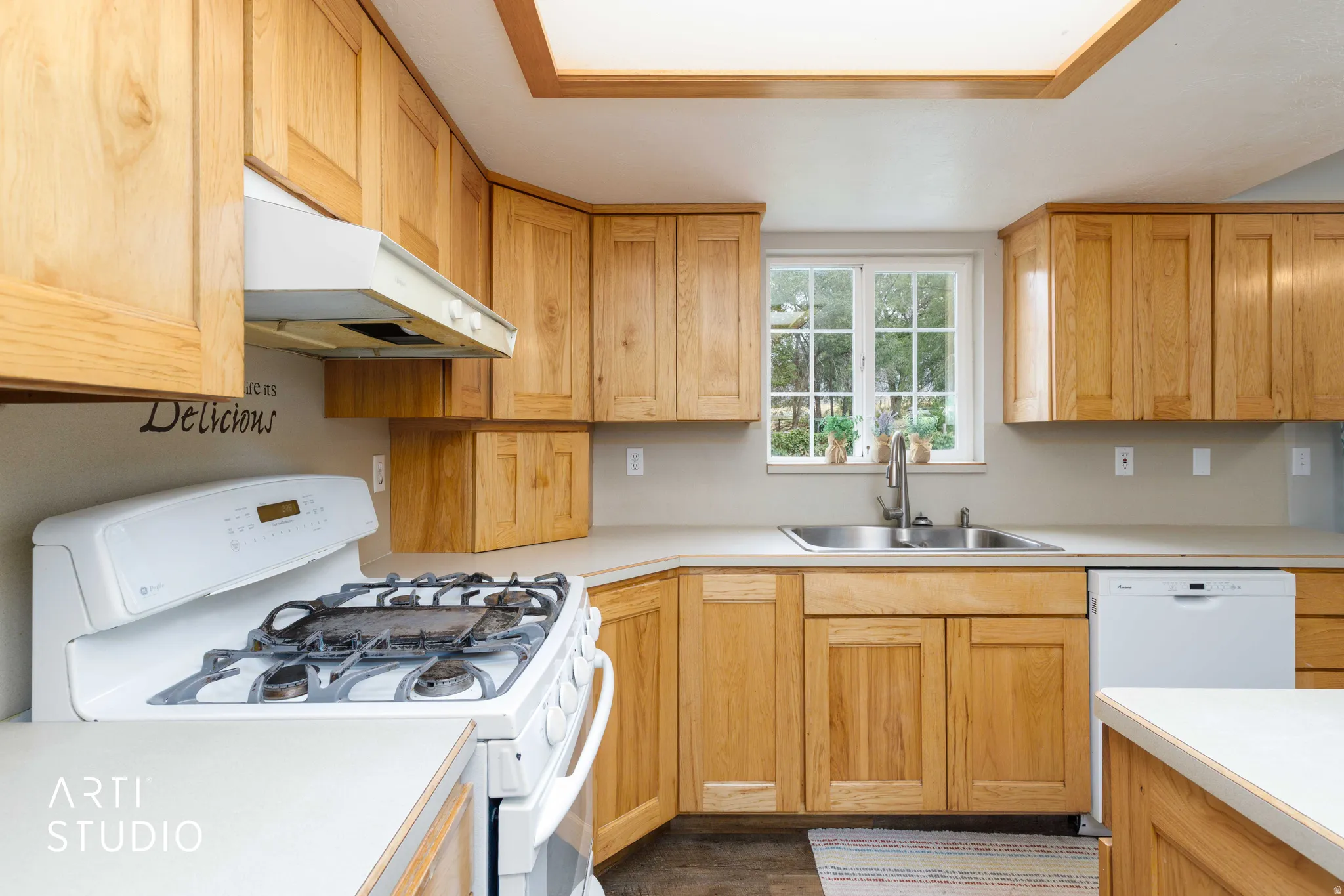 Wood cabinetry, solid surface countertops, stainless steel sink, built-in gas range, and a window with a garden grid