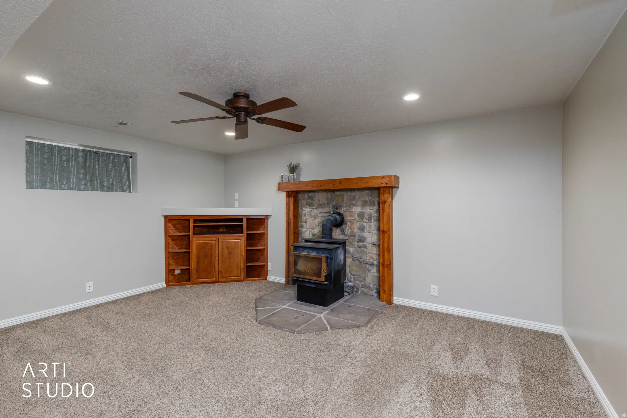 Built-in media center, stone-clad fireplace with wood stove, ceiling fan, recessed lighting, and carpeted flooring