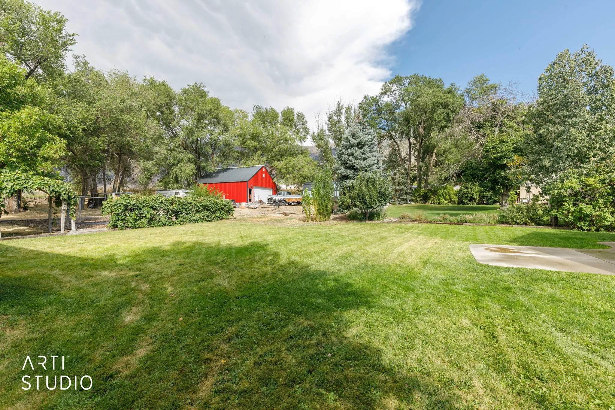 Expansive green lawn with mature trees and a red barn structure