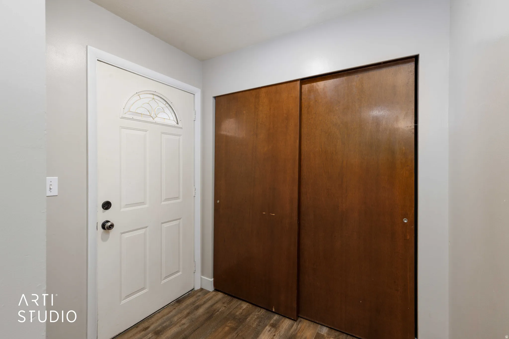 Entryway featuring a paneled door with decorative glass, wood-finish flooring, and a built-in closet with sliding wood doors