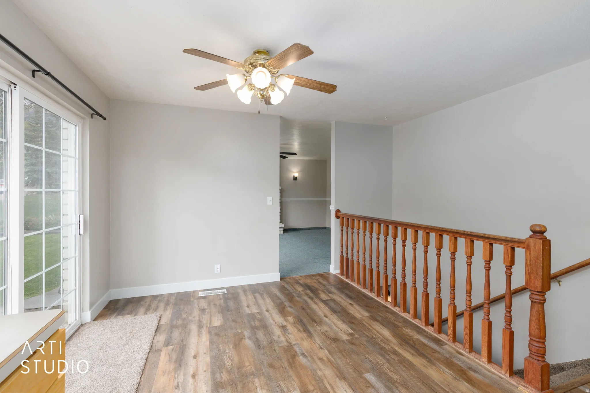 Wood-finish flooring, sliding glass door, overhead ceiling fan with lighting, and wood baluster railing