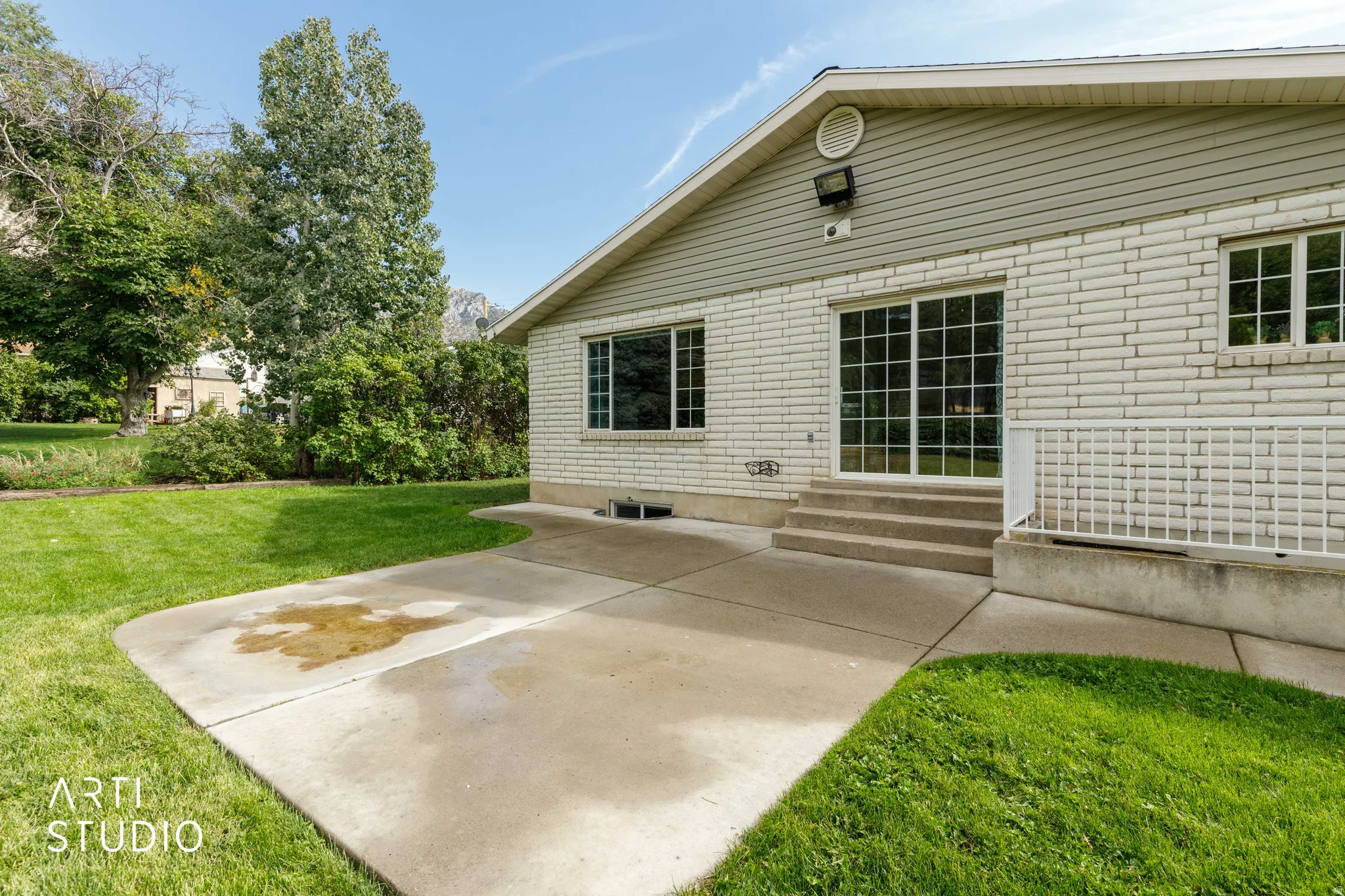 Expansive concrete patio with direct access to a sliding glass door, white brick exterior, and a large grassy area