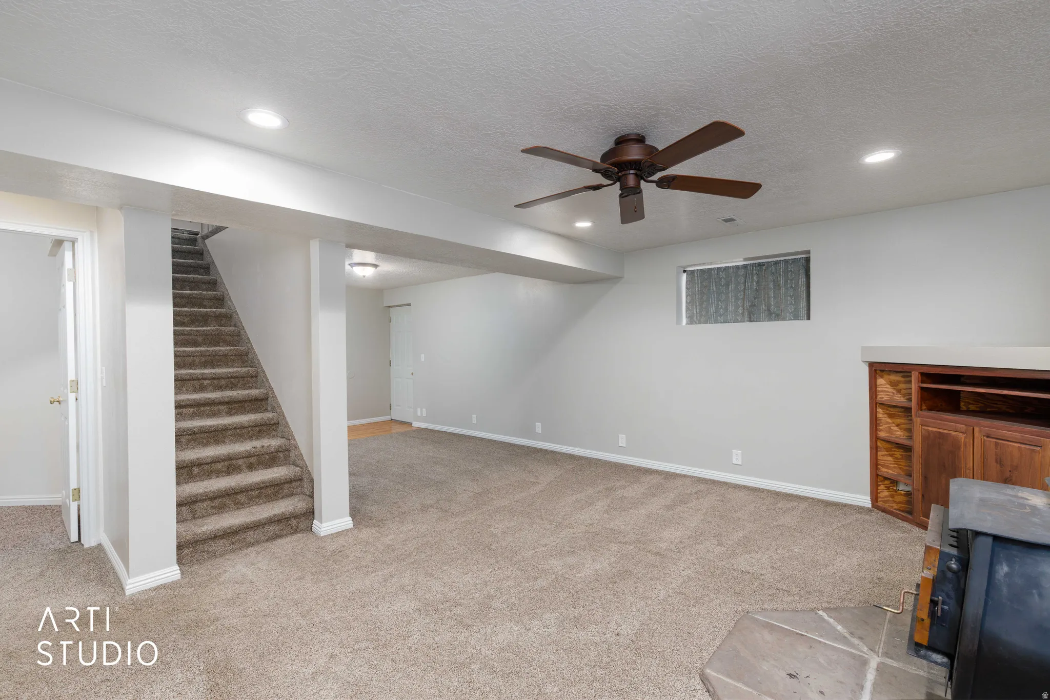 Expansive carpeted area featuring a wood-finish built-in entertainment unit, recessed lighting, and a ceiling fan