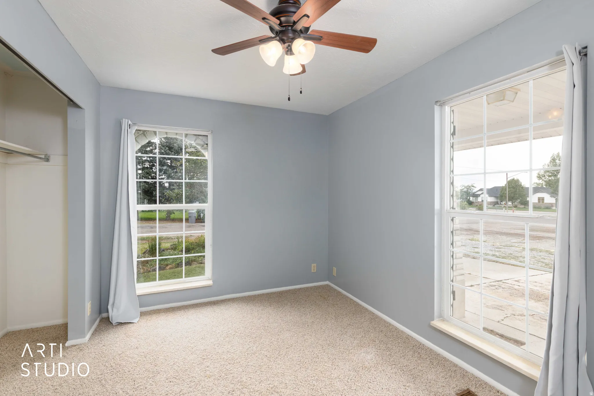 Soft neutral carpeting, two large windows, a built-in closet with hanging rod, and a ceiling fan with light fixture