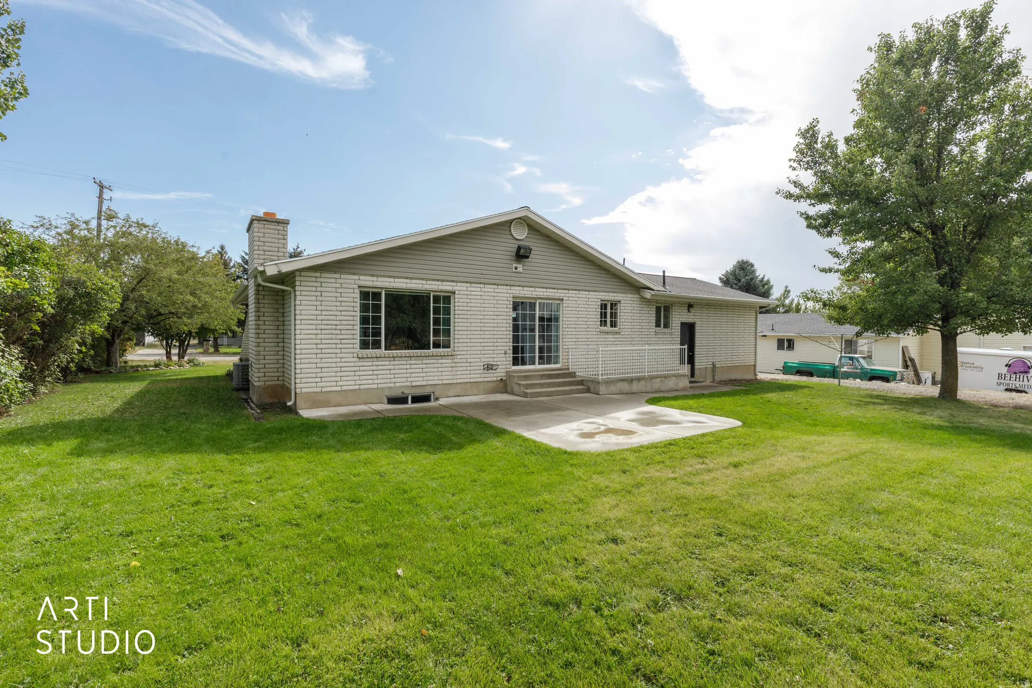 Brick exterior with siding accents, expansive green lawn, mature tree, and a concrete patio