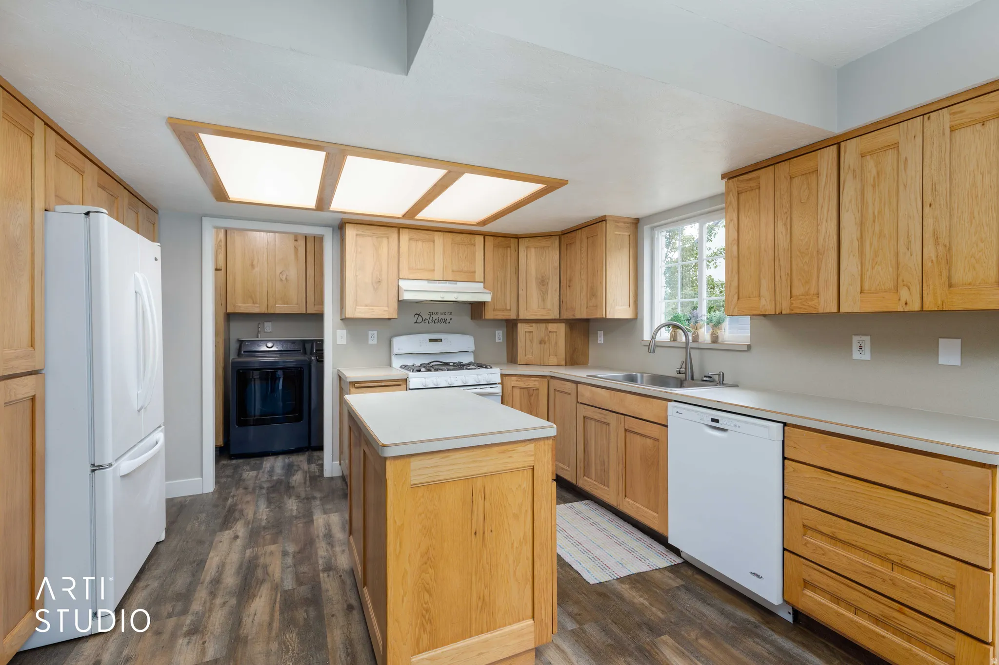 Kitchen featuring wood-finish cabinetry, light-toned countertops, wood-finish flooring, a central island, and an integrated ceiling light fixture