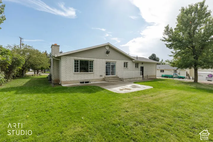 Brick exterior with siding accents, expansive green lawn, mature tree, and a concrete patio