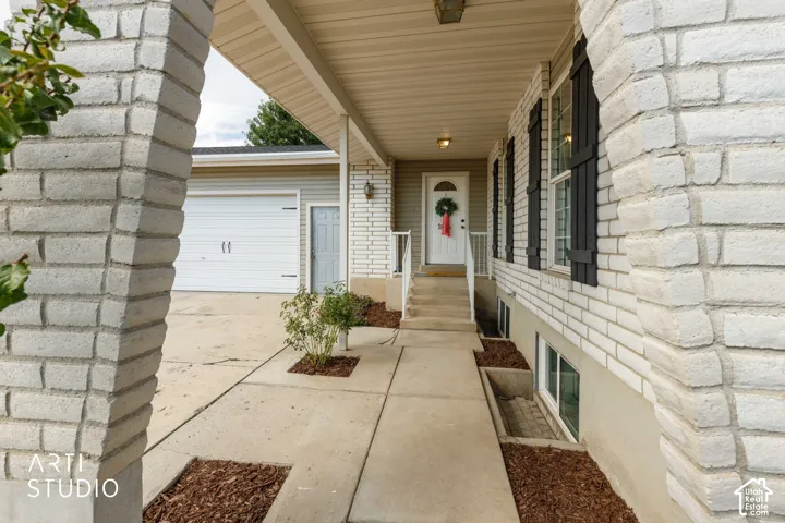 White brick exterior with black shutters, covered entry porch, concrete walkway, and a two-car garage