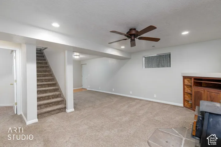 Expansive carpeted area featuring a wood-finish built-in entertainment unit, recessed lighting, and a ceiling fan