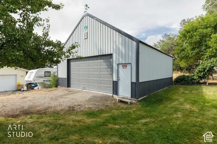 Metal sided shop featuring a gray overhead door, white side entry door, and a weather vane accent