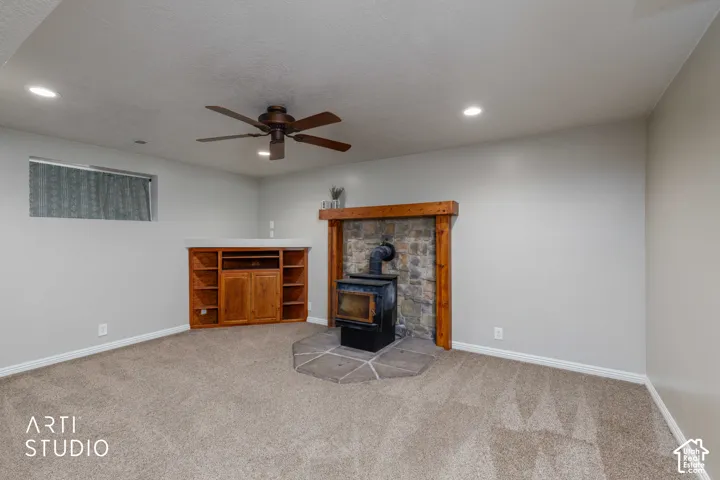 Built-in media center, stone-clad fireplace with wood stove, ceiling fan, recessed lighting, and carpeted flooring