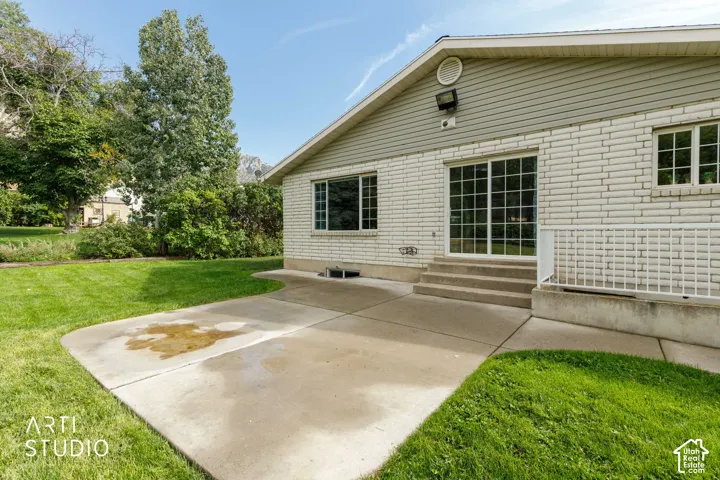 Expansive concrete patio with direct access to a sliding glass door, white brick exterior, and a large grassy area