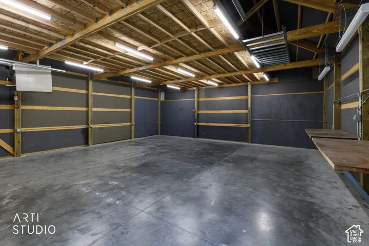 Spacious shop interior with exposed wood beam ceiling, multiple fluorescent light fixtures, concrete flooring, and built-in wooden work surfaces