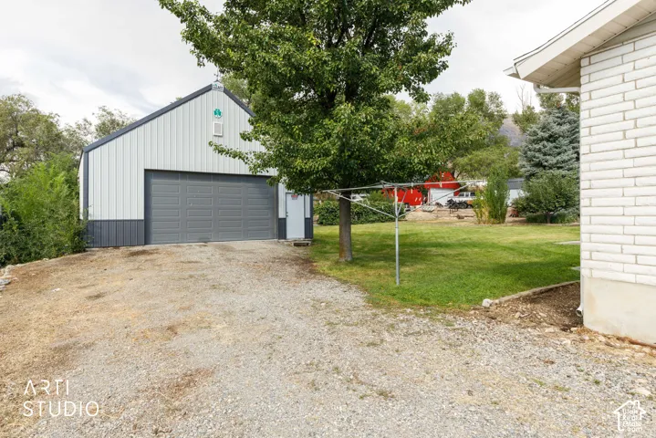 Detached 30 x 30 foot metal-sided shop with a large gray overhead door, gravel driveway, and a white brick-sided structure