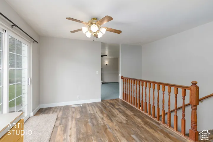Wood-finish flooring, sliding glass door, overhead ceiling fan with lighting, and wood baluster railing