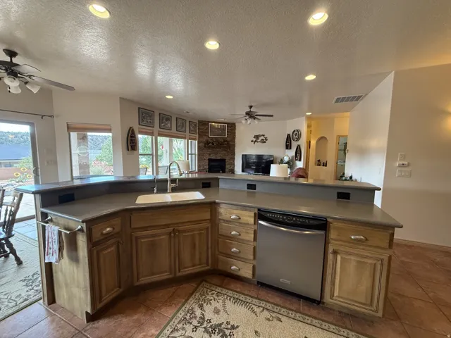Spacious kitchen island with integrated sink, stainless steel dishwasher, wood cabinetry, and ample counter space
