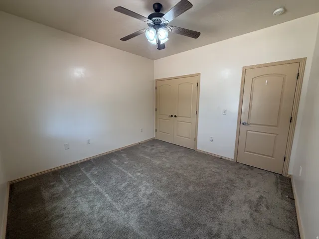 Neutral tone walls, ceiling fan with integrated lighting, gray carpeting, and two paneled doors with contrasting trim