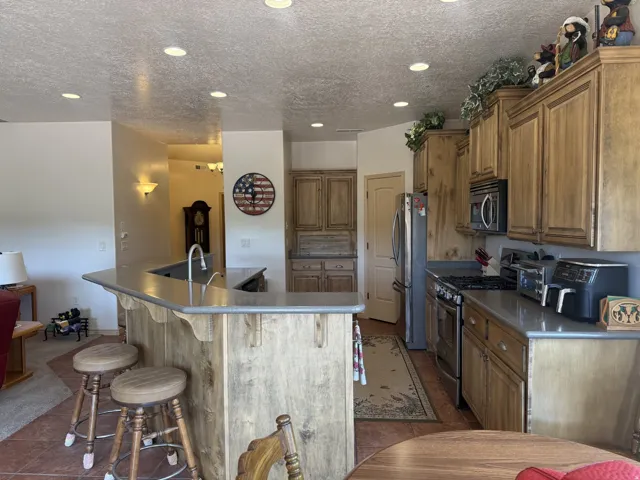 Kitchen featuring wood-finish cabinetry, built-in stainless steel appliances, a breakfast bar, recessed lighting, and tile flooring