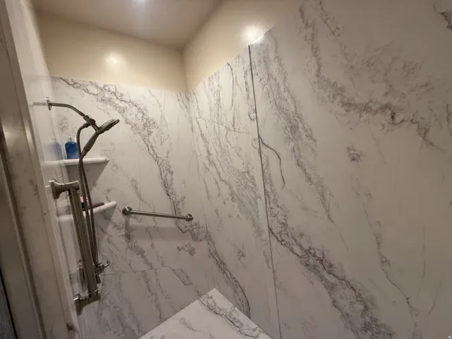 Shower with marbled-patterned wall panels, a built-in corner seat, and a brushed nickel shower fixture