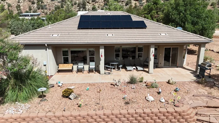 Rear exterior featuring a covered patio, solar panels, and a terraced xeriscape yard
