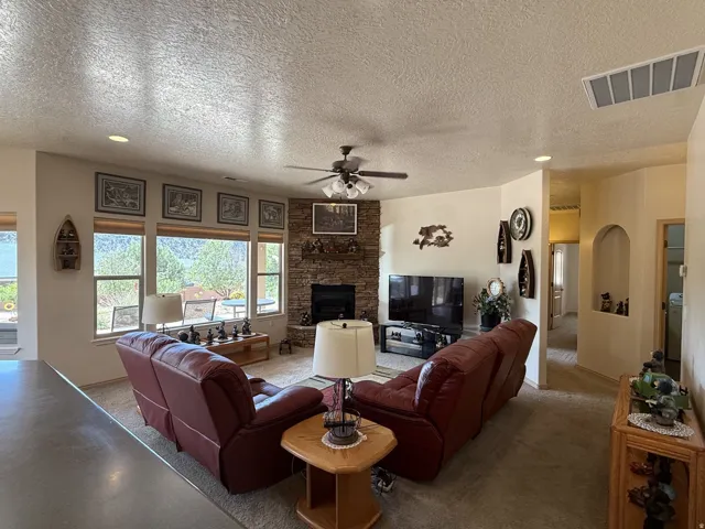Living area featuring a stone-faced fireplace, a multi-pane window wall, and a ceiling fan with integrated lighting