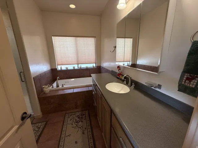 Soaking tub with tile surround, long vanity with integrated sink, and mirrored medicine cabinet