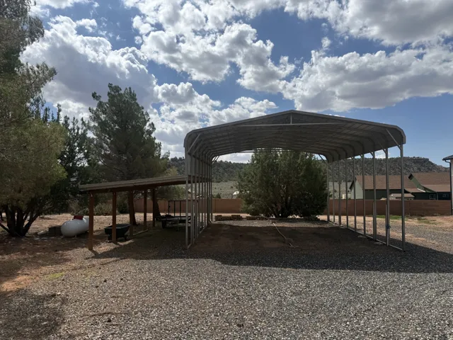 Gravel driveway leading to a large metal carport and a smaller covered structure