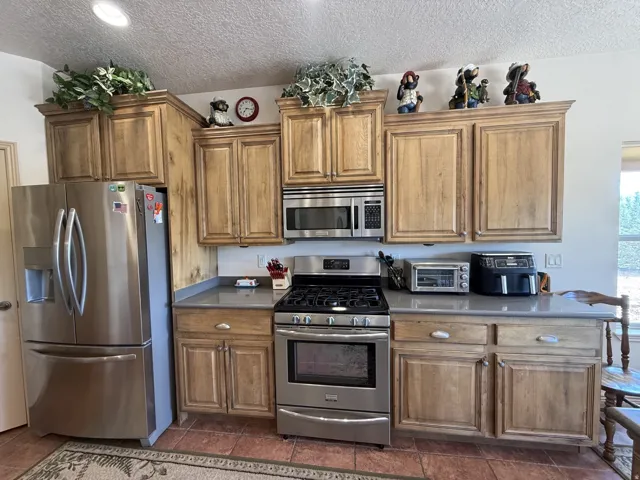 Stainless steel French door refrigerator, stainless steel microwave, stainless steel range, and light wood-finish cabinetry with light-toned countertops