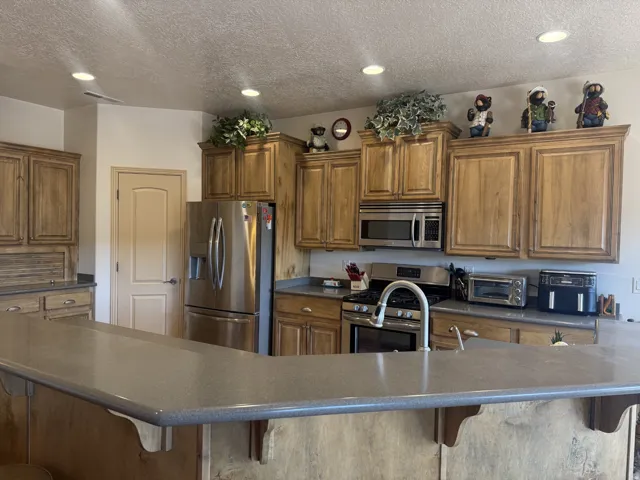 Kitchen featuring wood-finish cabinetry, stainless steel appliances, recessed lighting, and a breakfast bar with a solid surface countertop