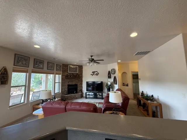 Living area featuring a stone-clad fireplace, recessed lighting, ceiling fan, and large windows