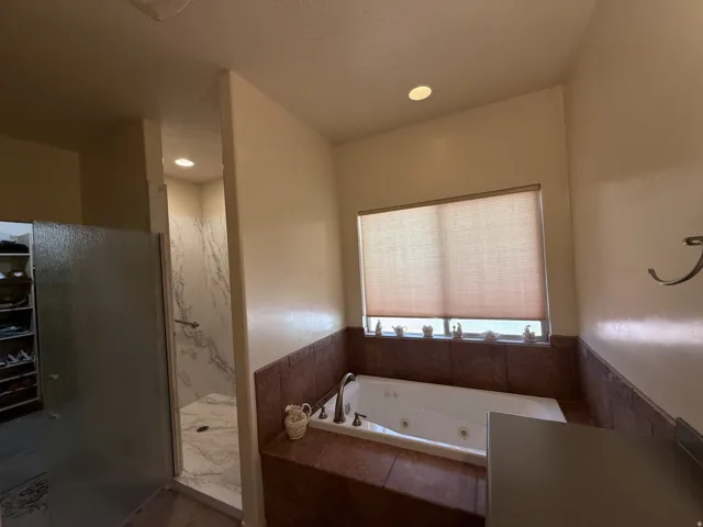 Jetted soaking tub with tile surround, walk-in shower with stone-finish walls and glass enclosure, and recessed lighting