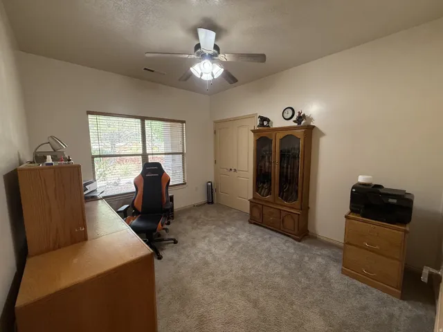 Vaulted ceiling with ceiling fan, dual windows with blinds, light-toned carpet flooring, and a paneled interior door