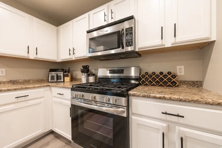 White cabinetry with black hardware, newer stainless steel gas range, built-in microwave, and LVP flooring