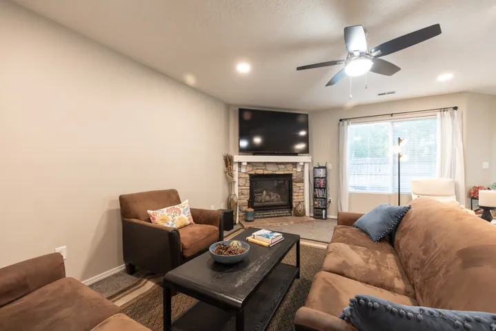 Family room featuring a built-in, gas log fireplace with stone surround, ceiling fan, recessed lighting, & a large window for beautiful views and natural light.