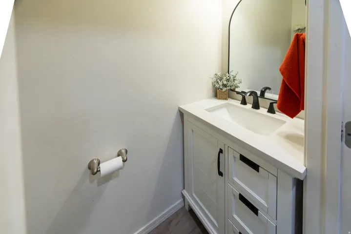 Main floor half bath features white vanity with shaker-style cabinetry, matte black hardware, solid surface counter top with square sink