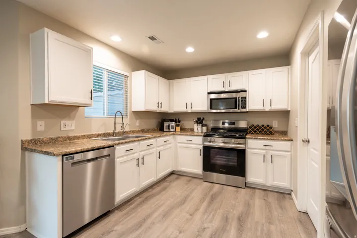 Kitchen featuring white cabinetry, newer stainless steel appliances, LVP flooring, recessed lighting, and a double basin sink
