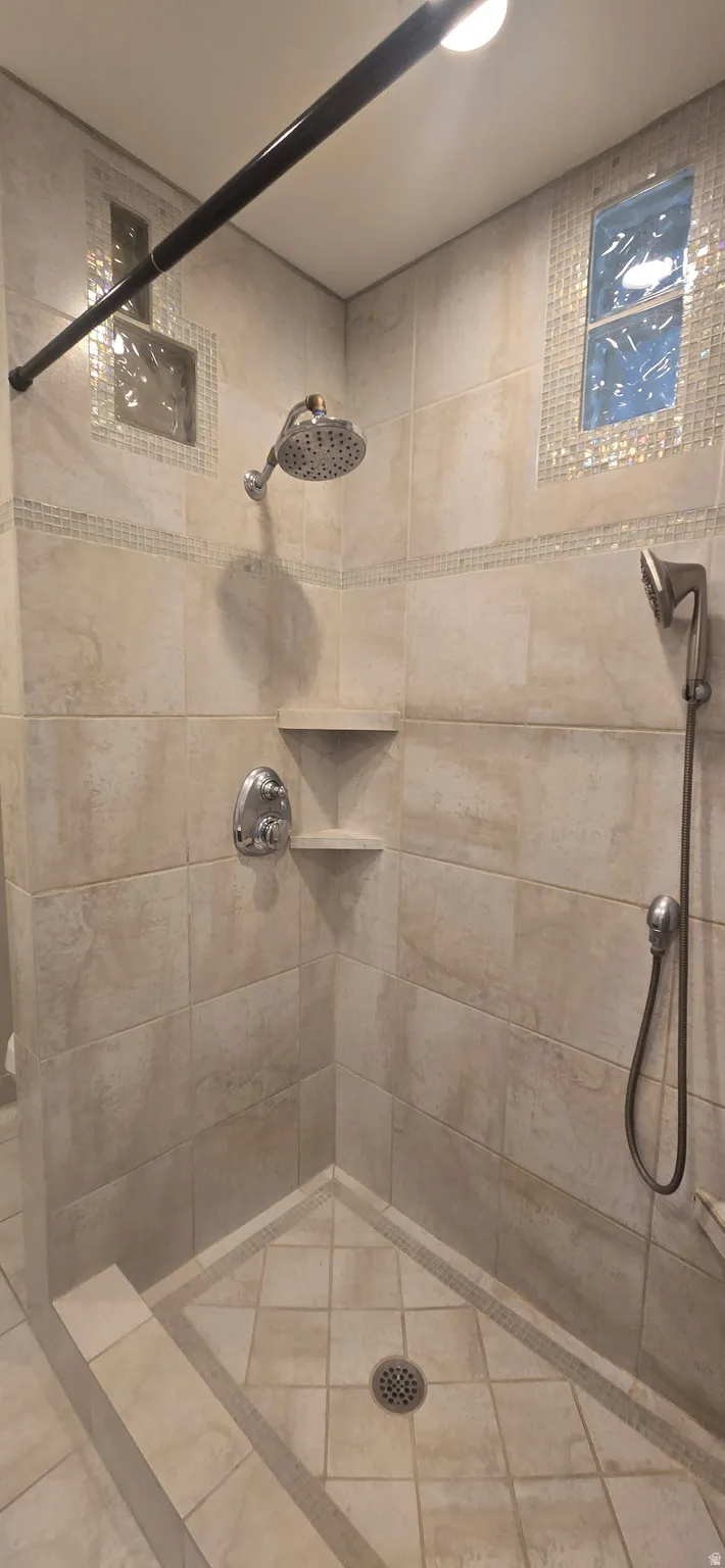 Tiled shower with a rain shower head, handheld shower fixture, built-in corner shelves, and mosaic accent tiling