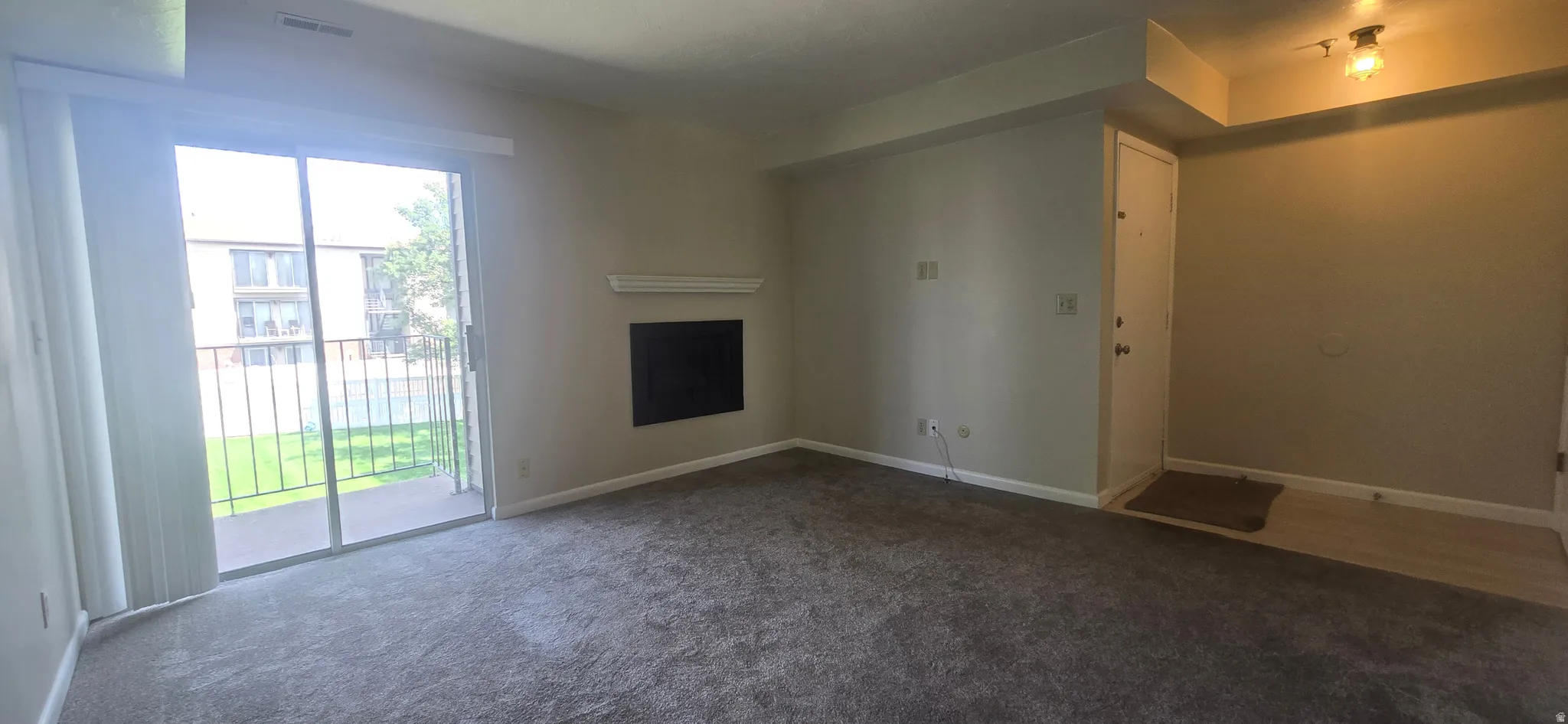 Sliding glass door, built-in fireplace with mantel, gray carpeting, front entry door, and track lighting fixture