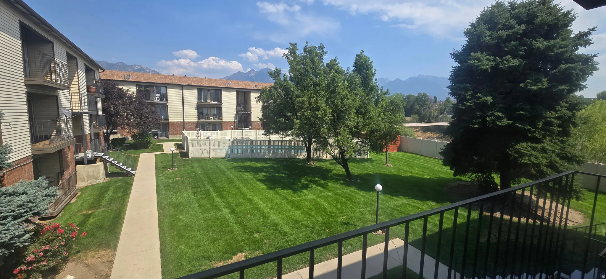 Expansive green space featuring a concrete pathway, mature trees, and mountainous scenery