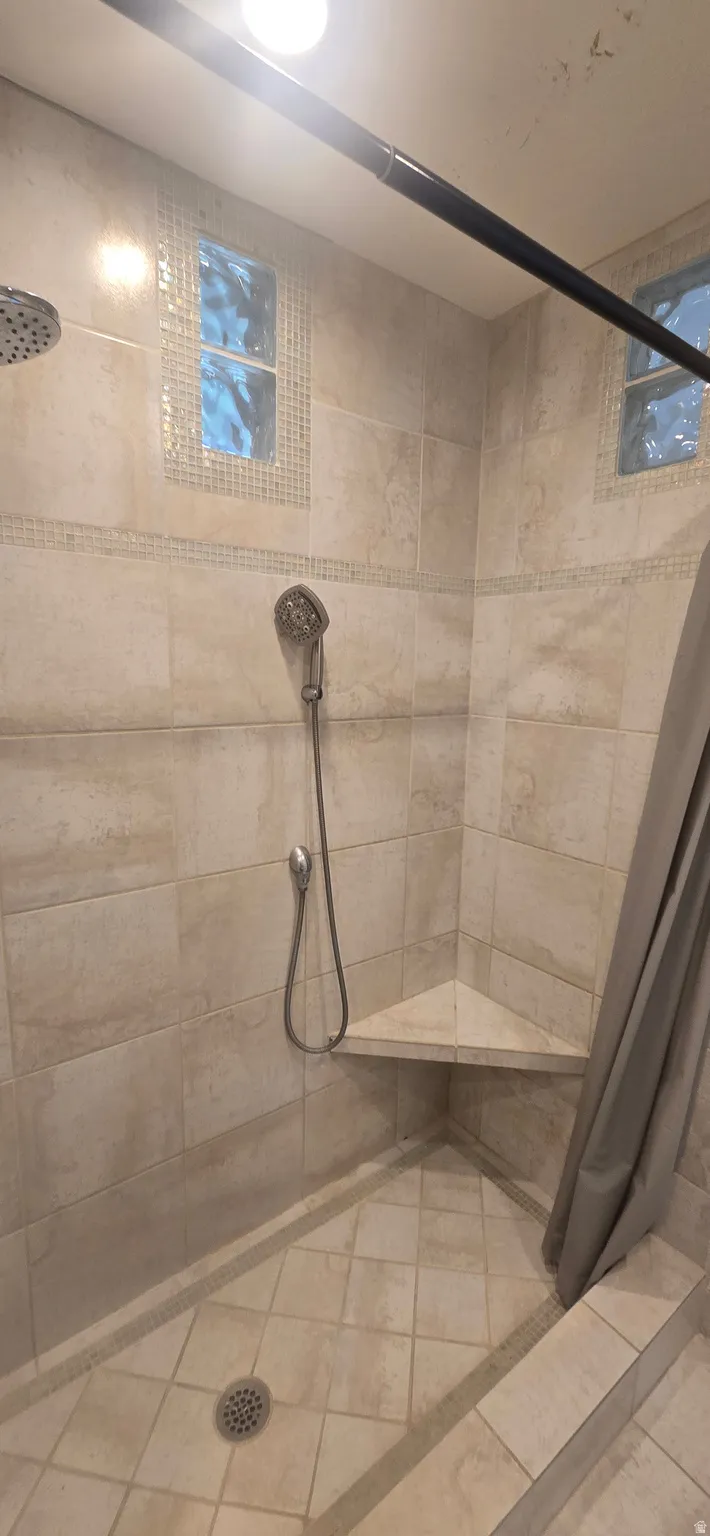 Tiled shower featuring a corner bench, handheld shower fixture, and recessed glass block windows