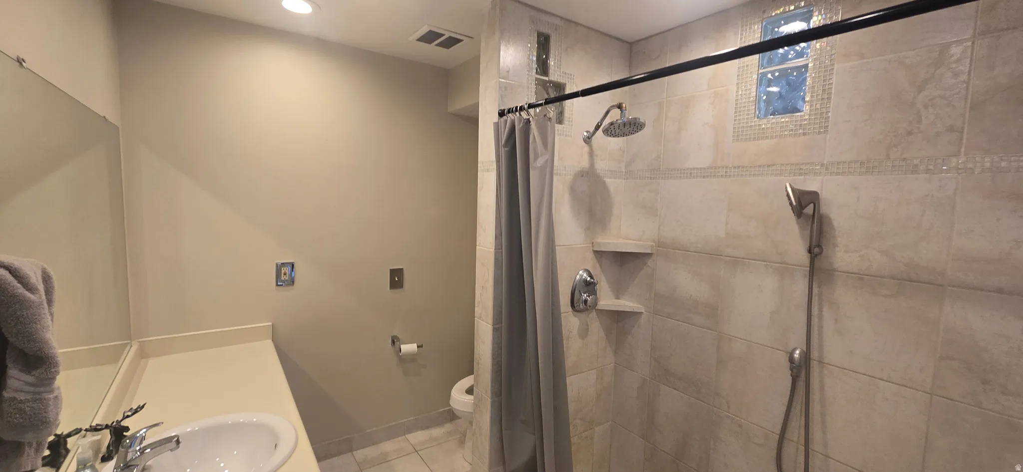 Recessed lighting, built-in vanity, tile shower with two shower heads, decorative tile accents, and an integrated shower window