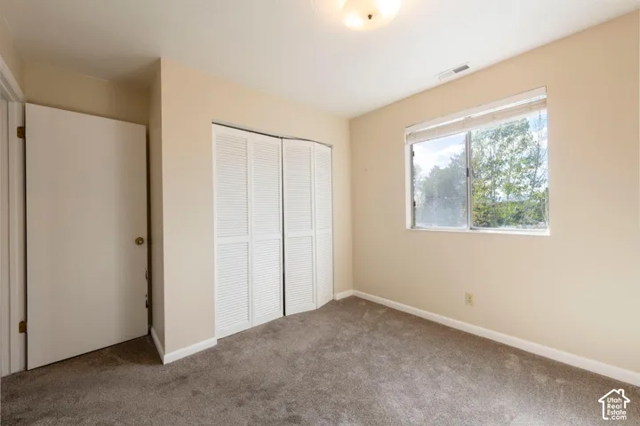 Neutral wall paint, gray carpet flooring, louvered bi-fold closet doors, and an overhead light fixture