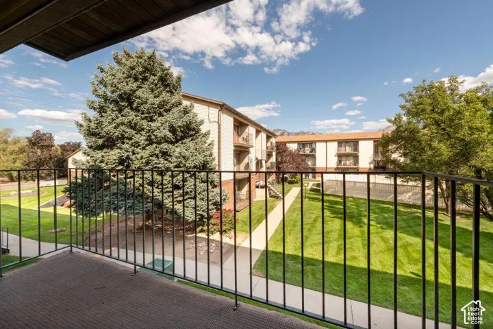 Private balcony with a metal railing, featuring a verdant lawn, mature trees, and landscaping