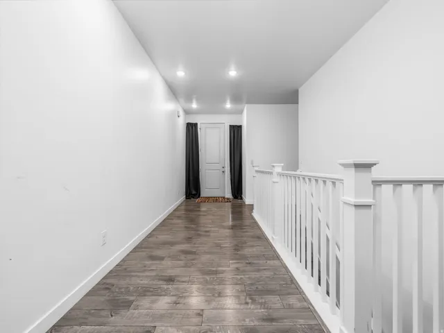 White interior walls, wood-finish flooring, recessed lighting, and white staircase railing