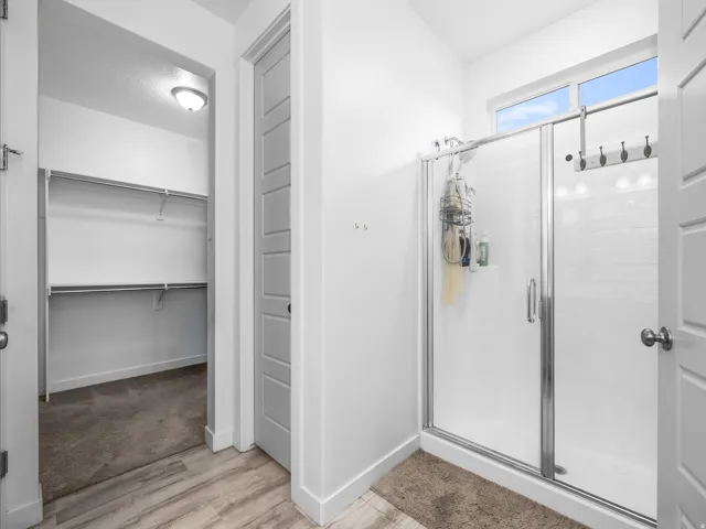 Walk-in closet with built-in shelving, glass-enclosed shower, transom window, and wood-finish flooring