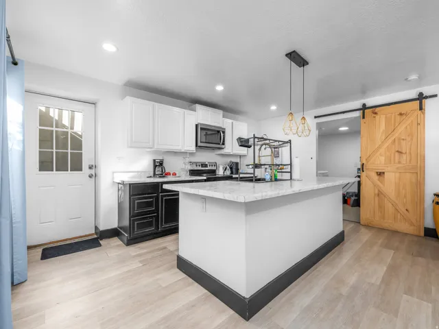 Kitchen with white upper cabinetry, black lower cabinetry, a center island with a white countertop, wood-finish flooring, and a sliding wood barn door