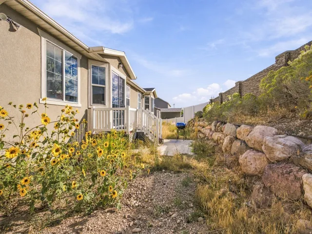 Stucco exterior with bay windows, white deck with railings, and an expansive stone retaining wall